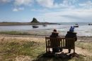 02D-2544 Two People Sitting on a Bench and Enjoying the View of Lindisfarne Castle Across the Ouse From the Harbour at Low Tide Holy Island Northumberland