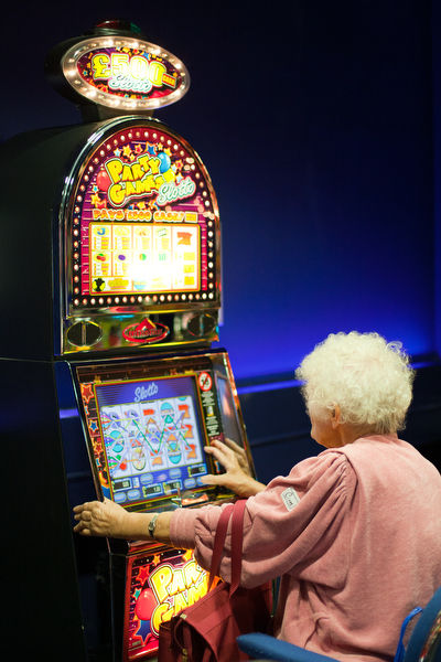After a few bingo games, an elderly woman tries her luck on a fruit machine