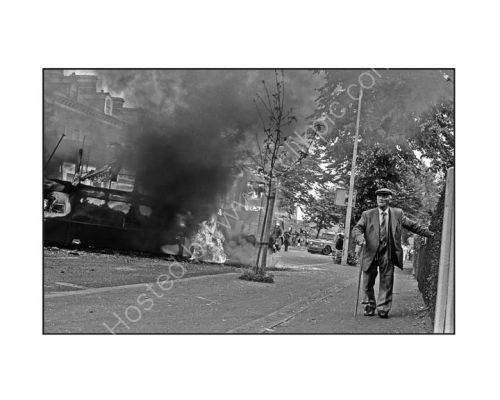 An ederly man attempts to walk up the Falls Road during fierce rioting.